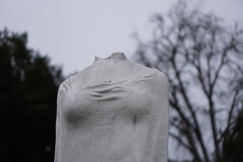 Marmorstatue, die eine aufrechtstehende weibliche Figur darstellt. Der Kopf fehlt, man erkennt nur noch die Bruchstelle.